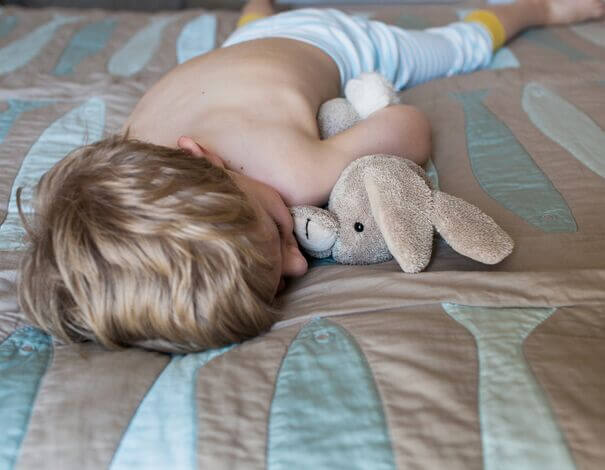 Toddler boy lying on bed, holding his stuffed animal