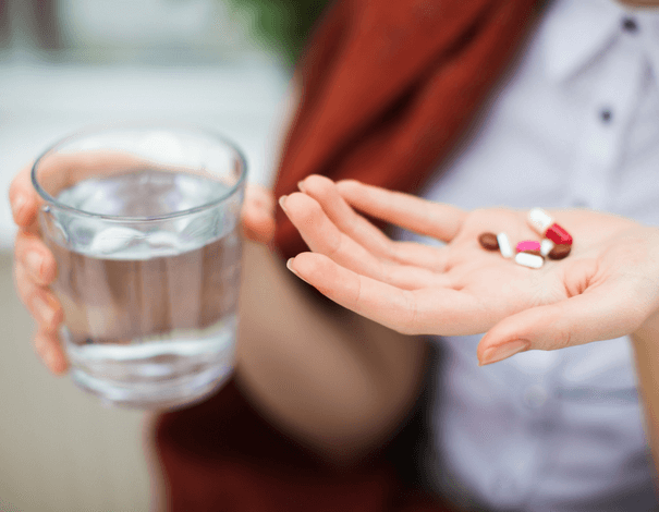 Woman's hand holding medication and a glass of water