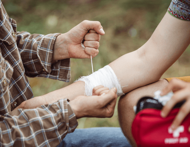 Personne mettant un bandage sur le bras blessé d'une autre personne à l'aide d'une trousse de premiers soins