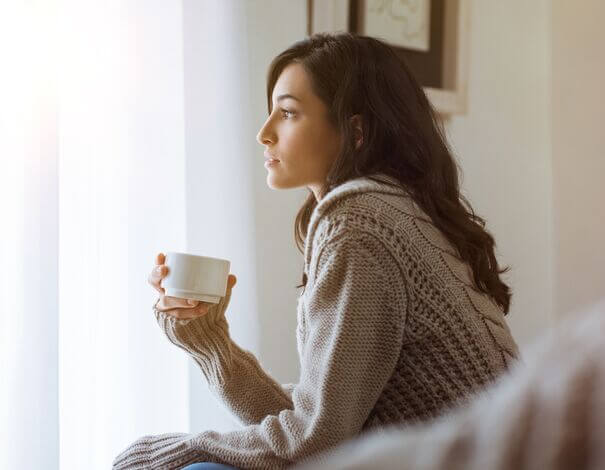 Jeune femme prenant un café et regardant par la fenêtre