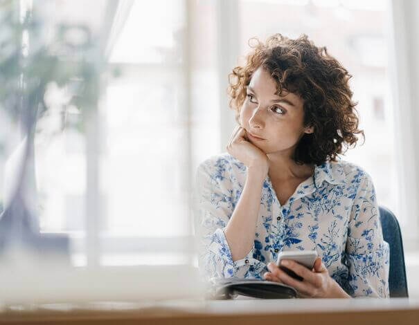 Jeune femme pensive tenant son téléphone en main