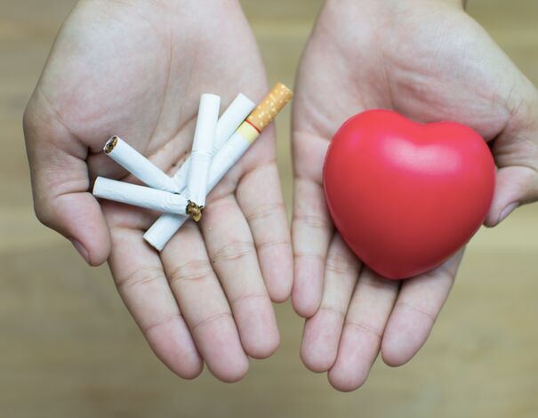 Une personne qui tient des cigarettes dans une main et dans l'autre main un coeur en plastique